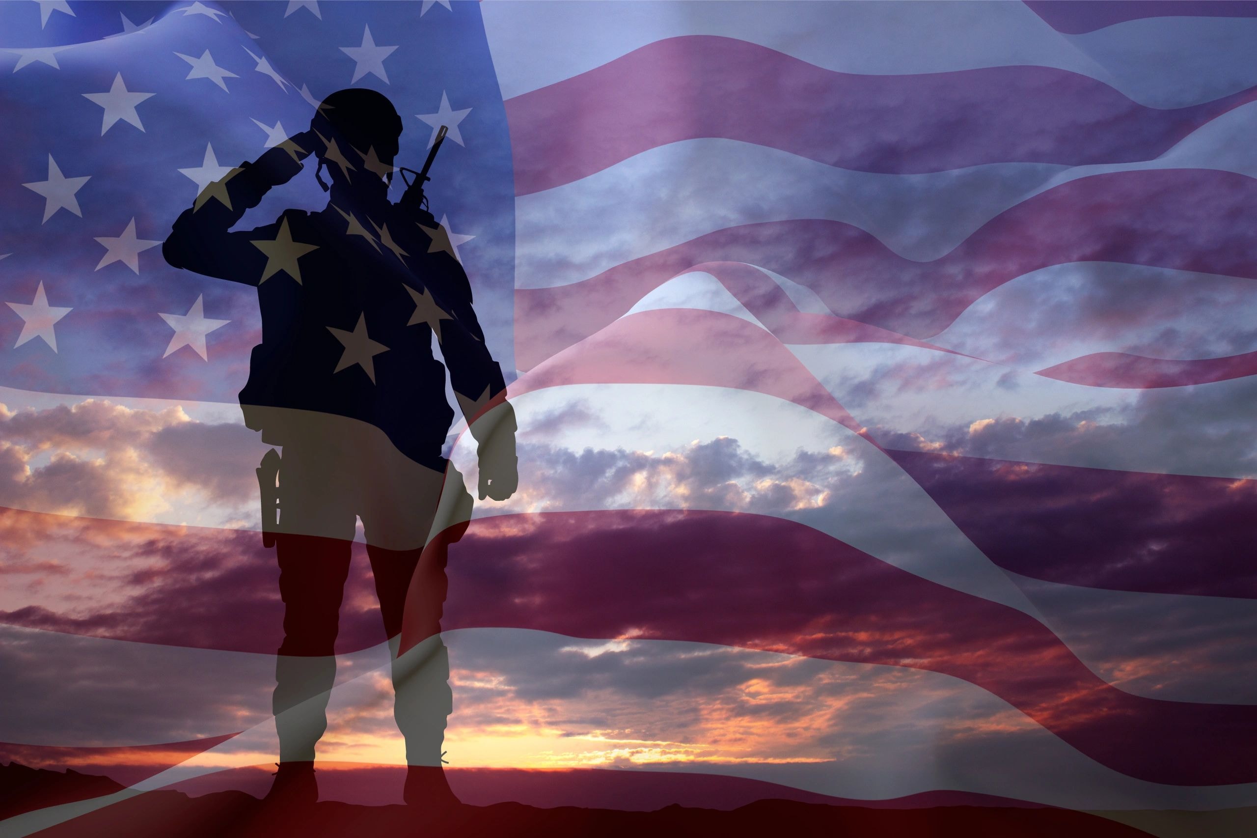 Silhouetted soldier with American flag at sunset